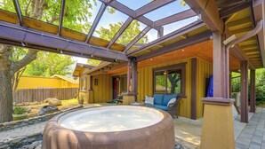 Un jacuzzi bajo techo de vidrio con una terraza de madera, bordeado por una cerca de piedra y un cerramiento de madera.