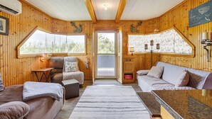 L’intérieur d’un chalet accueillant, avec des murs en bois, une grande fenêtre, un canapé, une table à manger et un petit coin cuisine.