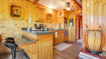Un intérieur en bois comprenant un coin cuisine, des tabourets de bar et une lampe décorative.