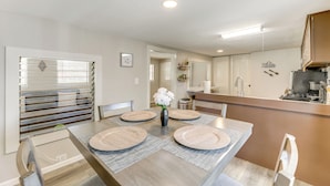 Een moderne keuken met een centraal eiland, een eethoek met een tafel voor vier personen, en uitzicht op de aangrenzende woonkamer.