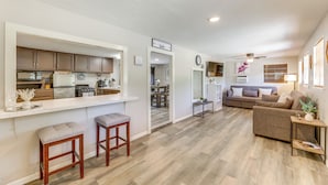 Een moderne keuken met een bar, een woonkamer met een bank en een salontafel, en een eethoek met een tafel en stoelen.