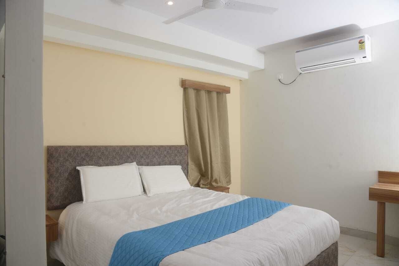 Una camera d'albergo con un letto, una ventola a soffitto, un condizionatore d'aria e un comodino in legno.