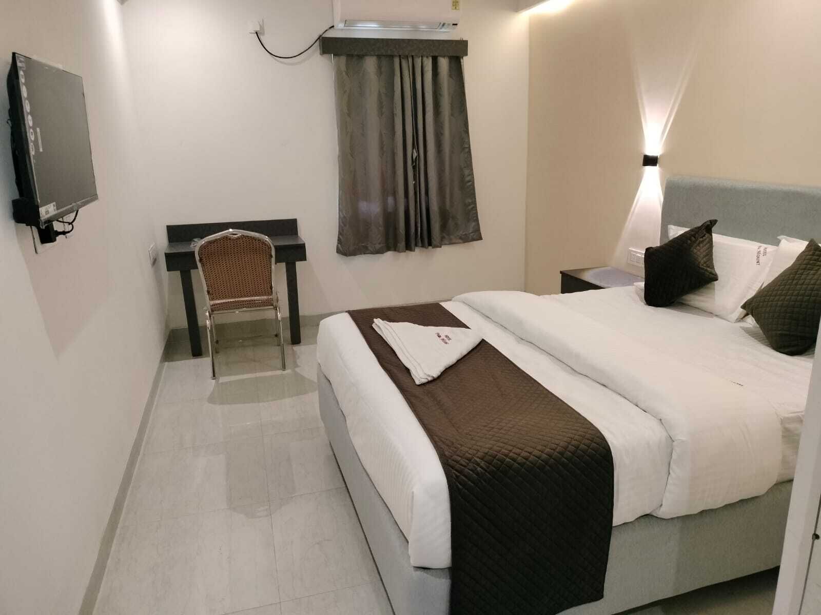 A hotel room with a bed, a desk, a chair, a TV, and a window with curtains.