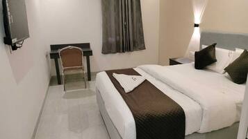 A hotel room with a bed, a desk, a chair, a TV, and a window with curtains.