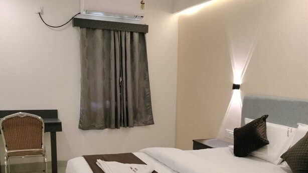 A hotel room with a bed, a chair, a desk, and an air conditioning unit. - Hotel Paramount (Visakhapatnam)