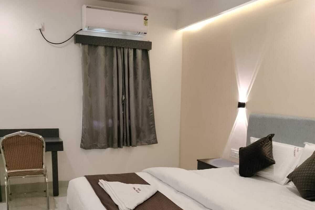 A hotel room with a bed, a chair, a desk, and an air conditioning unit.