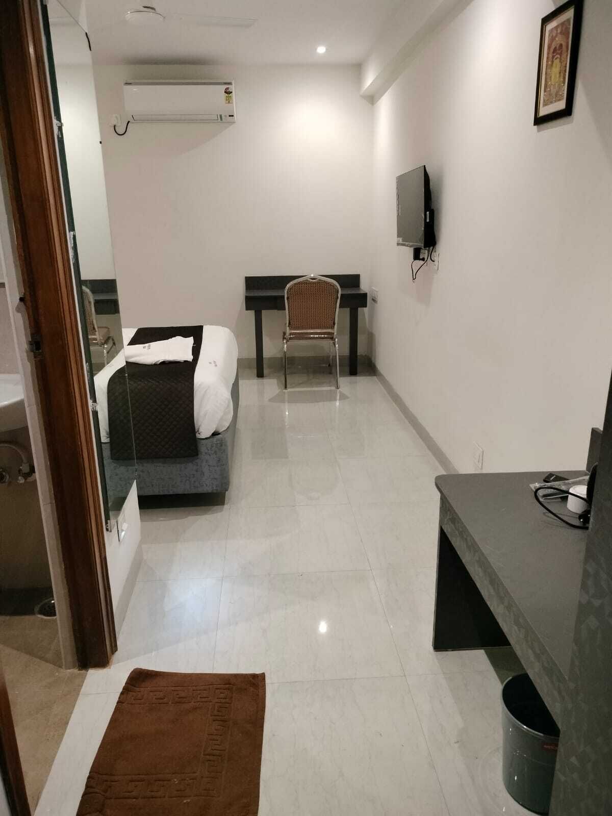 A hotel room with a bed, a desk, a chair, a television, and a bathroom visible through an open door.