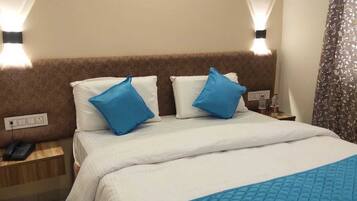 A hotel room with a bed, two pillows, a bedside table with a phone, and a wall-mounted light fixture.