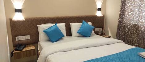 Una habitación de hotel con una cama, dos almohadas, una mesita de noche con un teléfono y una lámpara fijada a la pared.