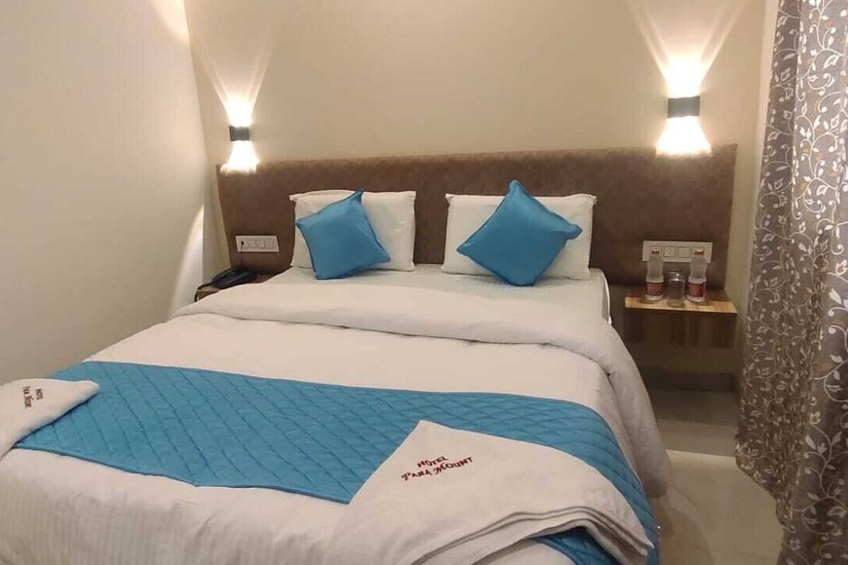 A hotel room with a bed, two bedside tables, a nightstand, a blue blanket, and a floral curtain.