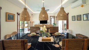 A dining area with a black marble table, woven pendant lights, and wooden chairs. - Villa Lange 2 by Villa Finder (Seminyak)