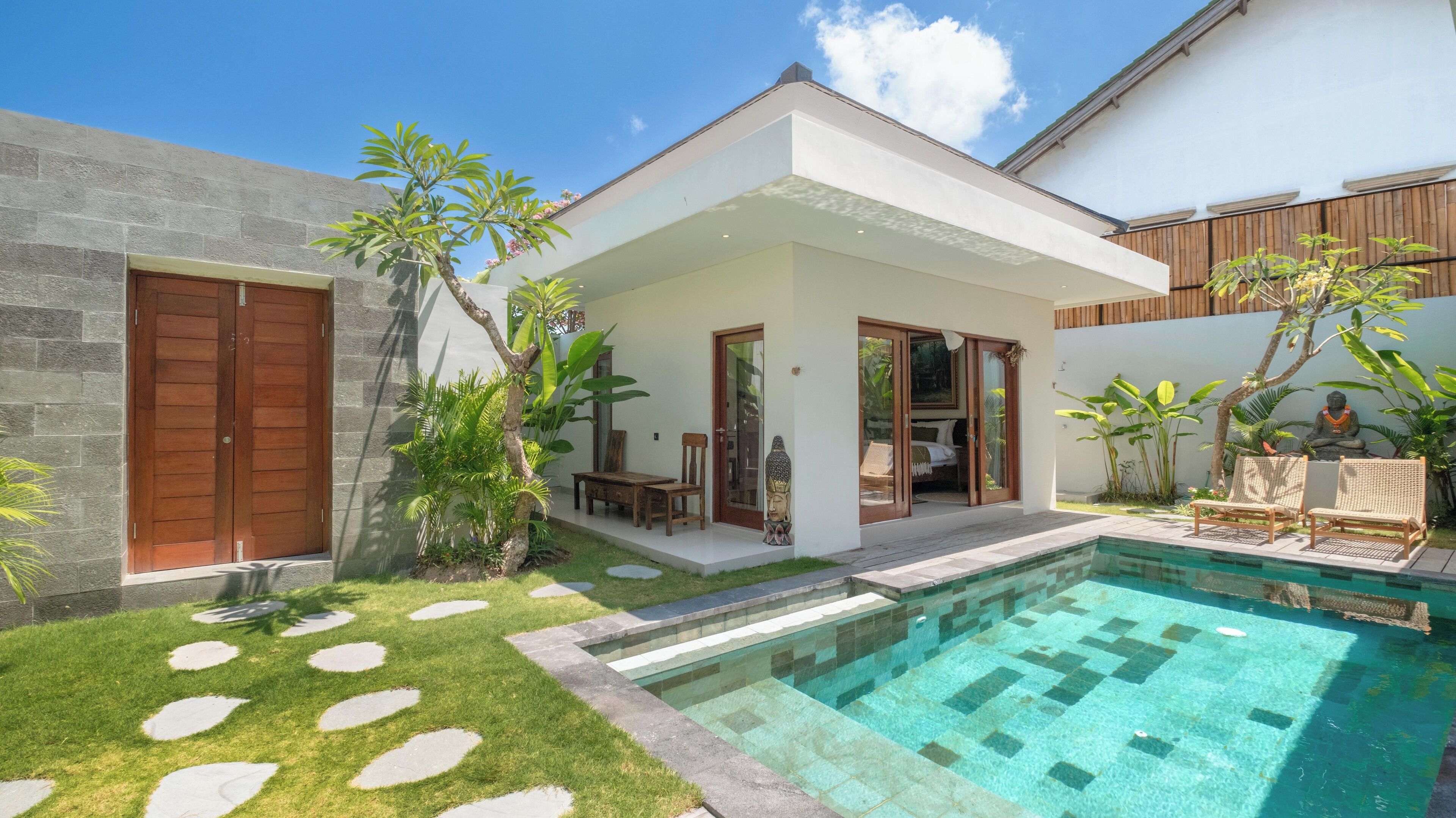 A modern house with a swimming pool, a patio with seating, and a Buddha statue.