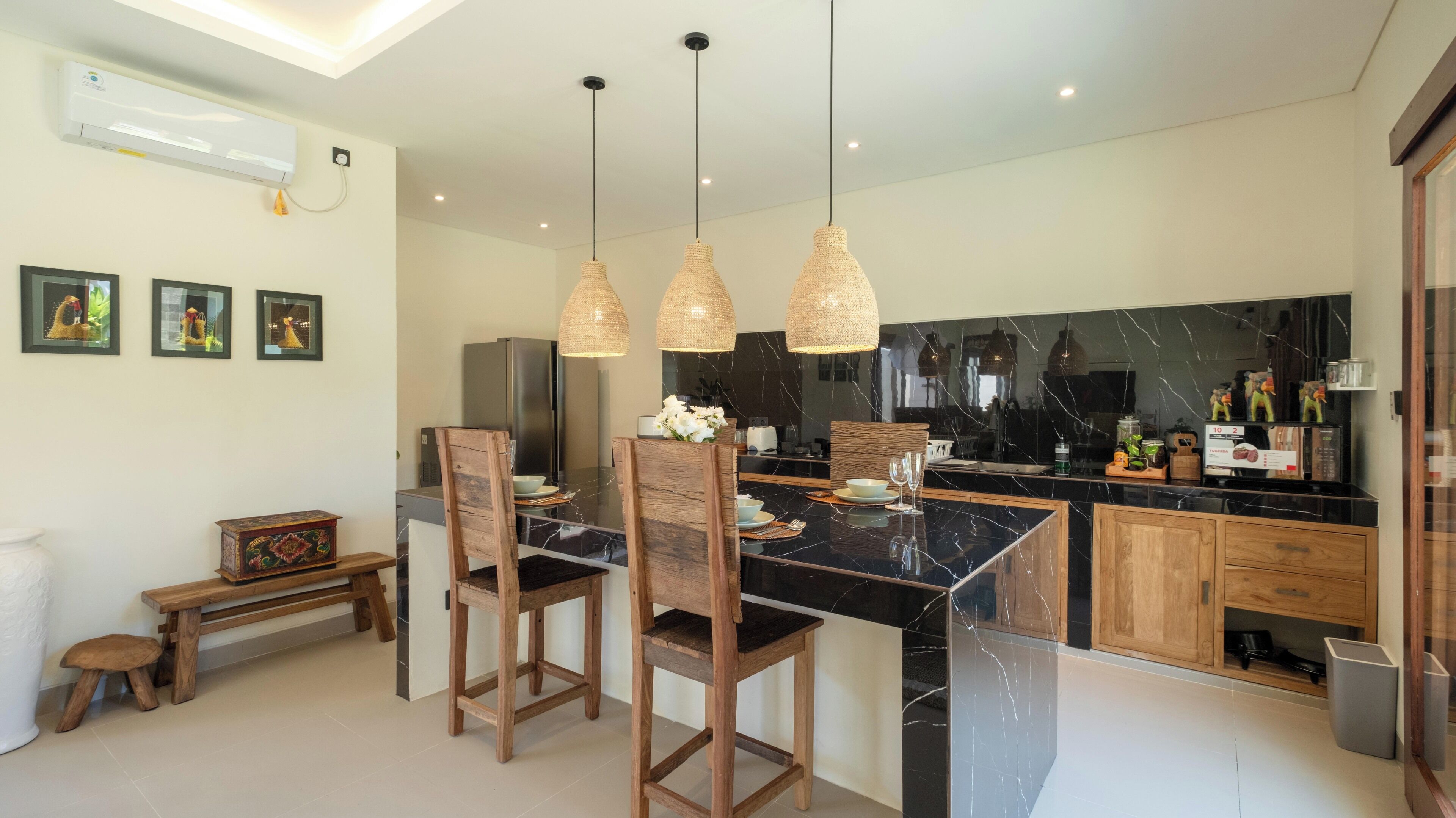 A modern kitchen with a marble countertop, wooden chairs, and pendant lights.