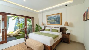 A bedroom with a large bed, a sliding glass door to a balcony, a painting on the wall, and a small bedside table. - Villa Lange 2 by Villa Finder (Seminyak)