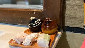 Un plateau en bois avec deux récipients en céramique et un objet emballé, le tout posé sur un comptoir blanc.