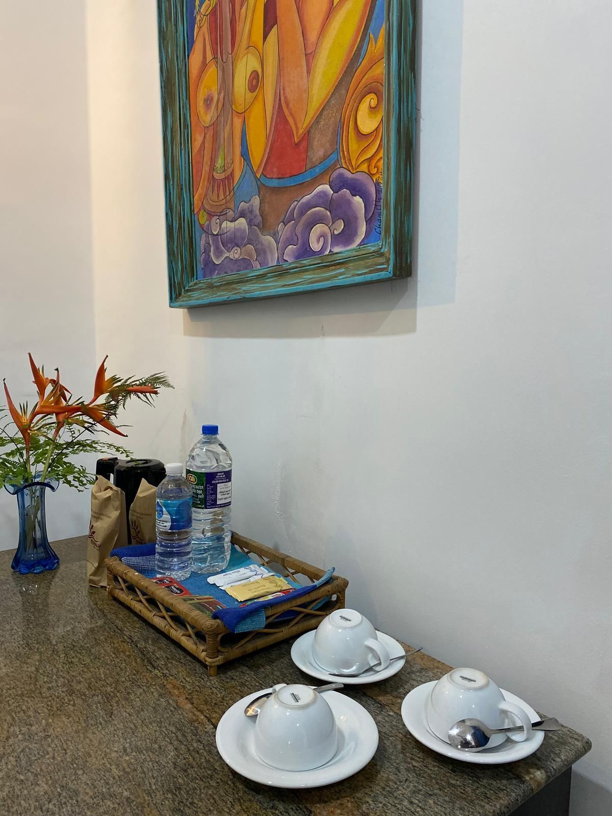 A dining area with a table set for tea, a painting on the wall, and a plant in a vase.