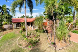 Una casa con techo rojo, rodeada de un jardín cuidado con diversas plantas y árboles.