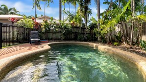 A clear swimming pool surrounded by a wooden fence, with a chair and a small table nearby.