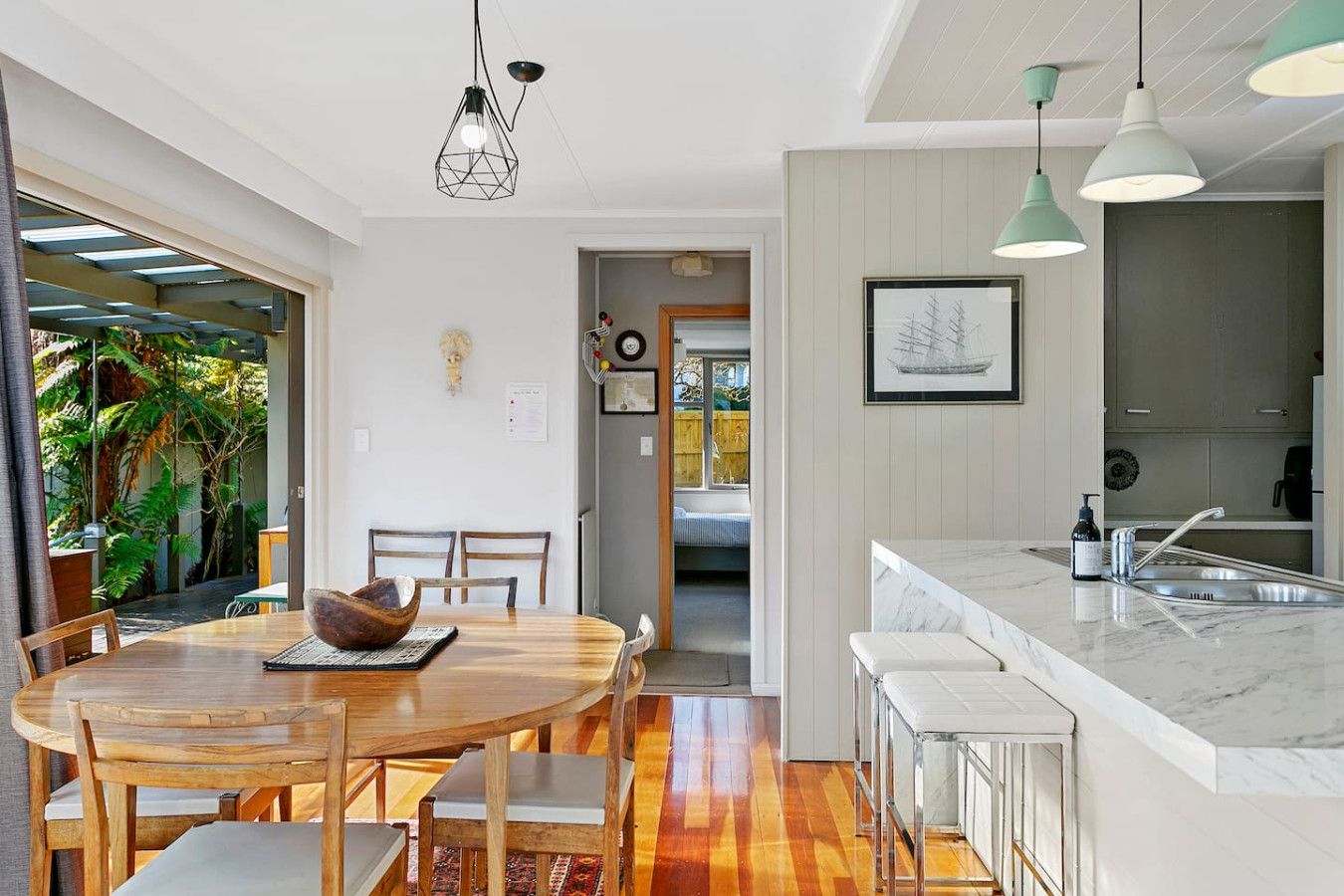 A modern kitchen with a marble countertop, wooden dining table, and pendant lighting.