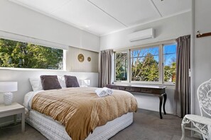 A hotel room with a large bed, a desk, a chair, and a window with a view of trees.
