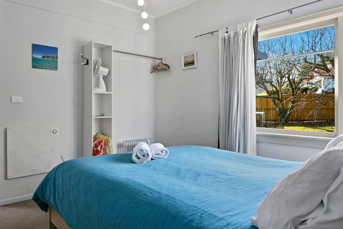 Quarto com cama, radiador, varal e janela com cortinas.