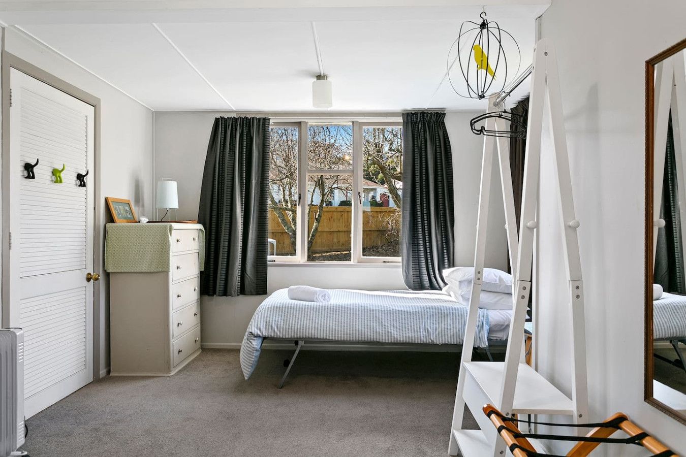 Un dormitorio con cama, cómoda, espejo y ventana con cortinas.