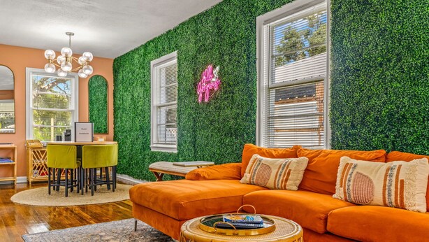 Ein Wohnzimmer mit grüner Wand, einem orangefarbenen Sofa und einem runden Tisch mit Tablett.