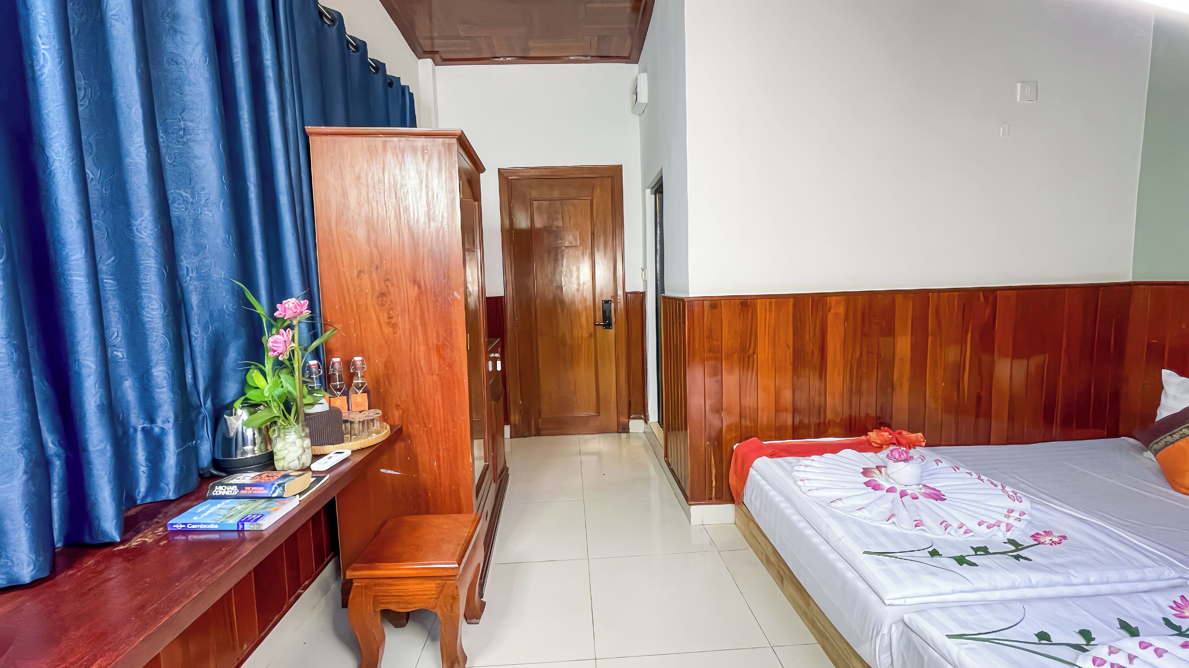 Camera d'albergo con un'armadiatura in legno, una scrivania con un vaso di fiori, un letto con copriletto floreale e una tenda blu.