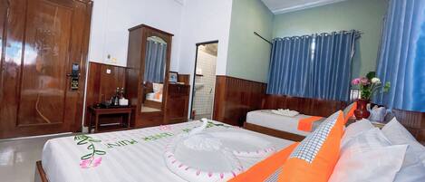A hotel room with a large bed, a smaller bed, a wooden wardrobe, a desk with a chair, and a bathroom visible through an open door.
