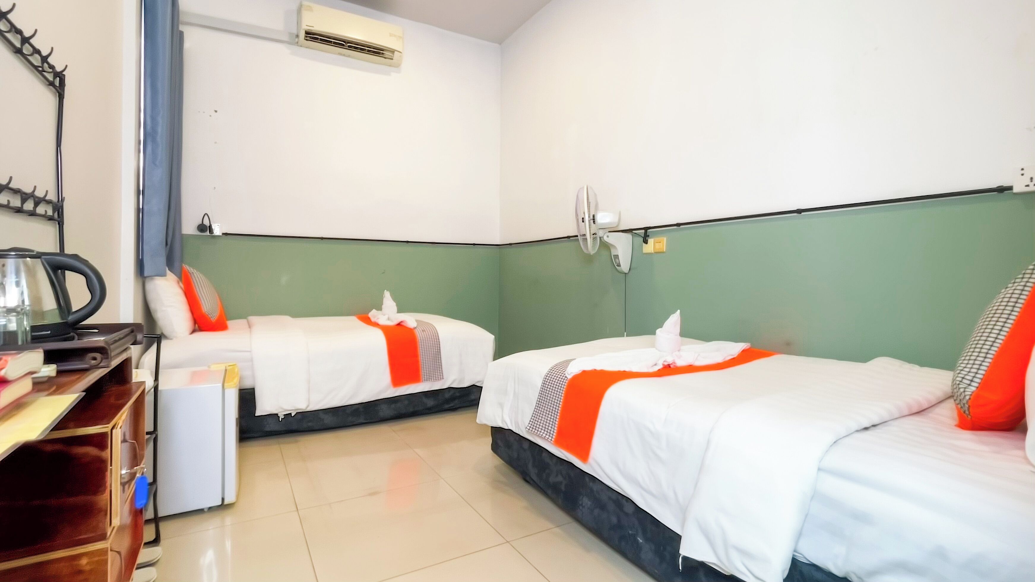 A hotel room with two beds, a desk with a kettle, a telephone, and an air conditioning unit.