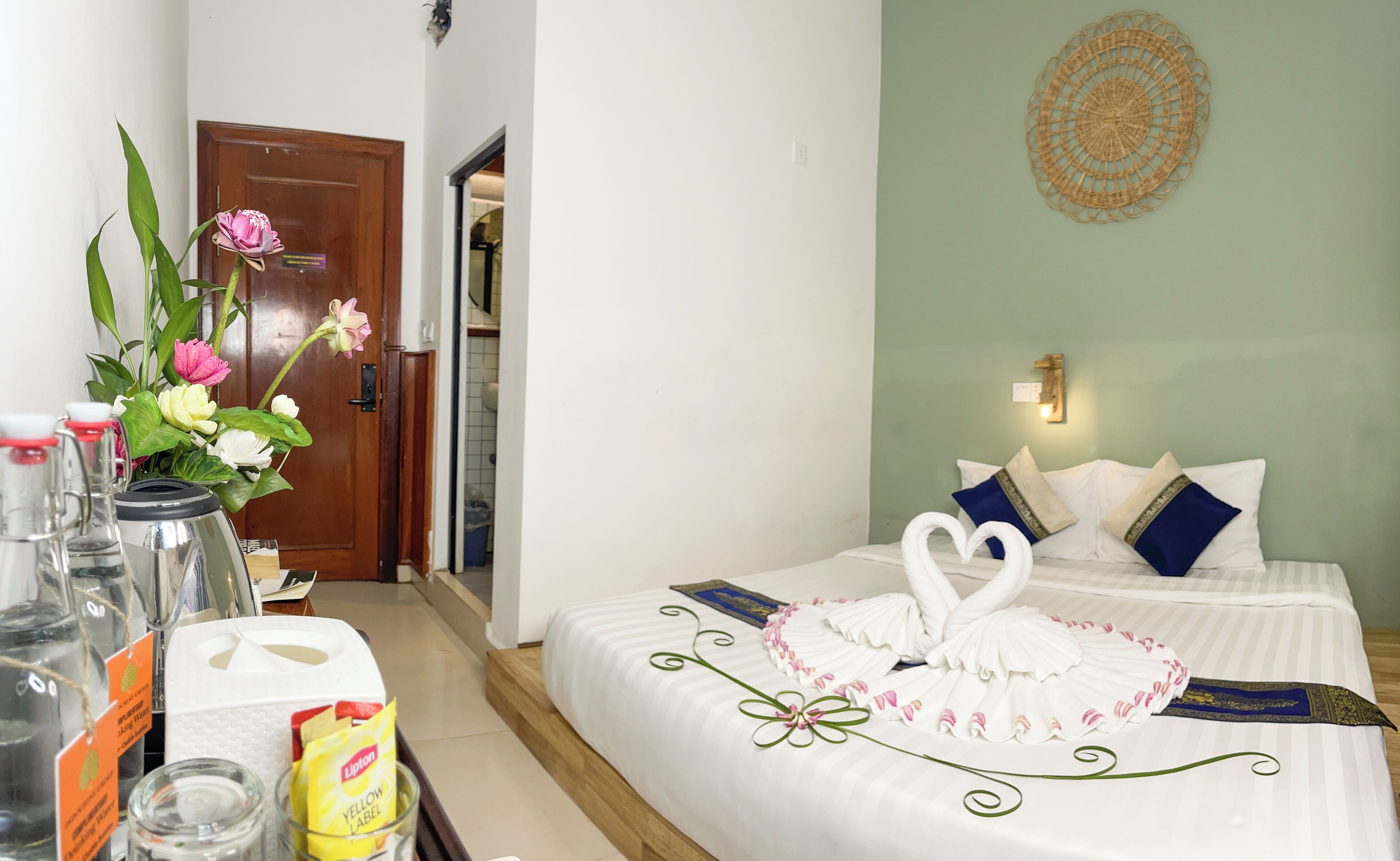A hotel room with a bed, a wall decoration, and a vase with flowers.