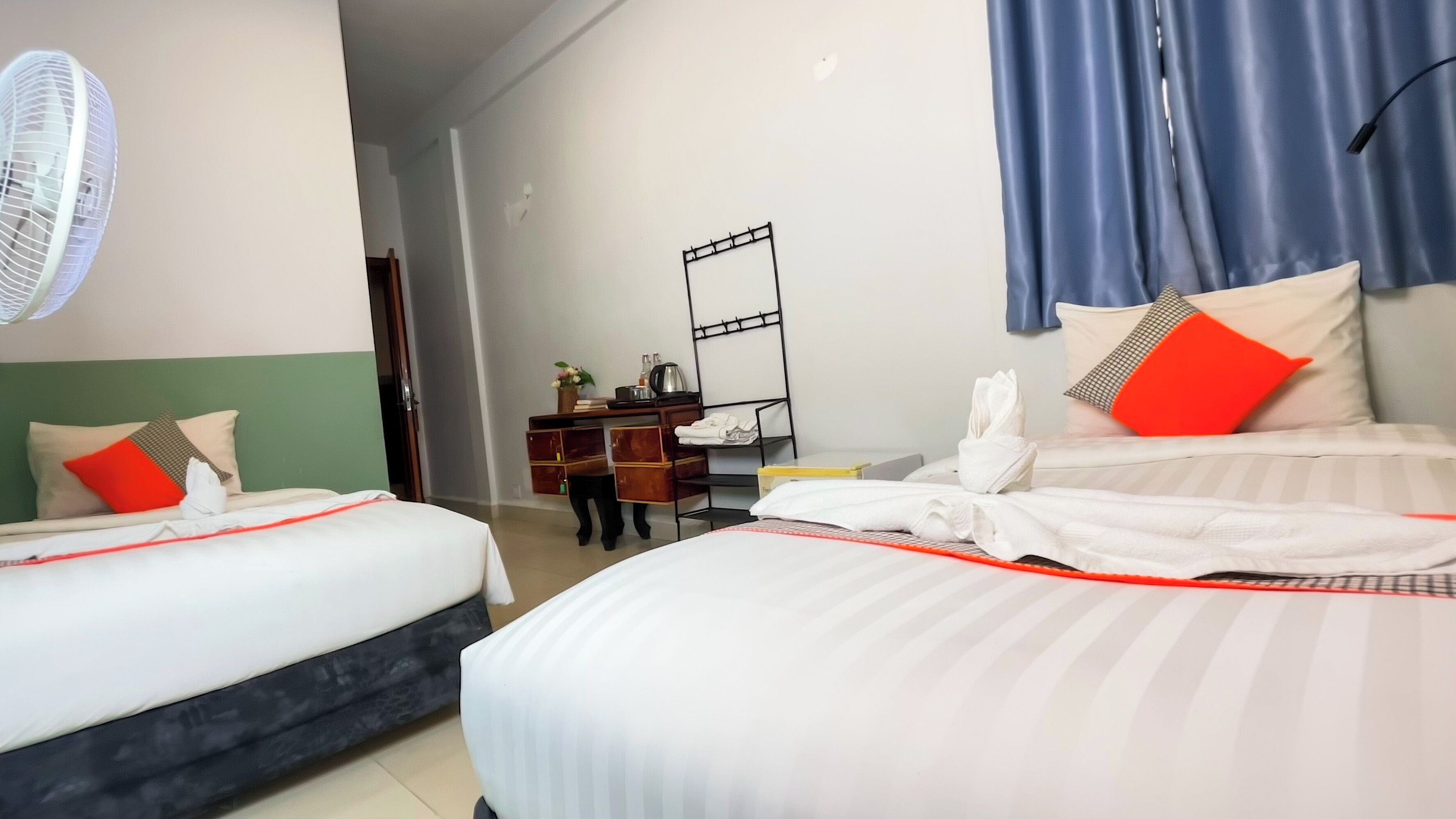 Habitación de hotel con dos camas, un escritorio, una silla, un espejo y un ventilador.