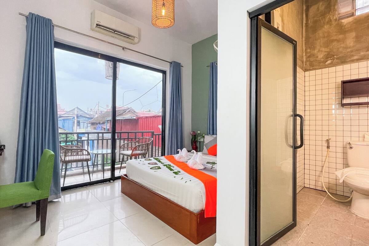 A hotel room with a balcony, a bed, a desk, and a bathroom.