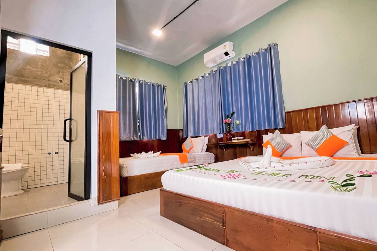 A hotel room with a large bed, two smaller beds, a shower area, and a wooden headboard.