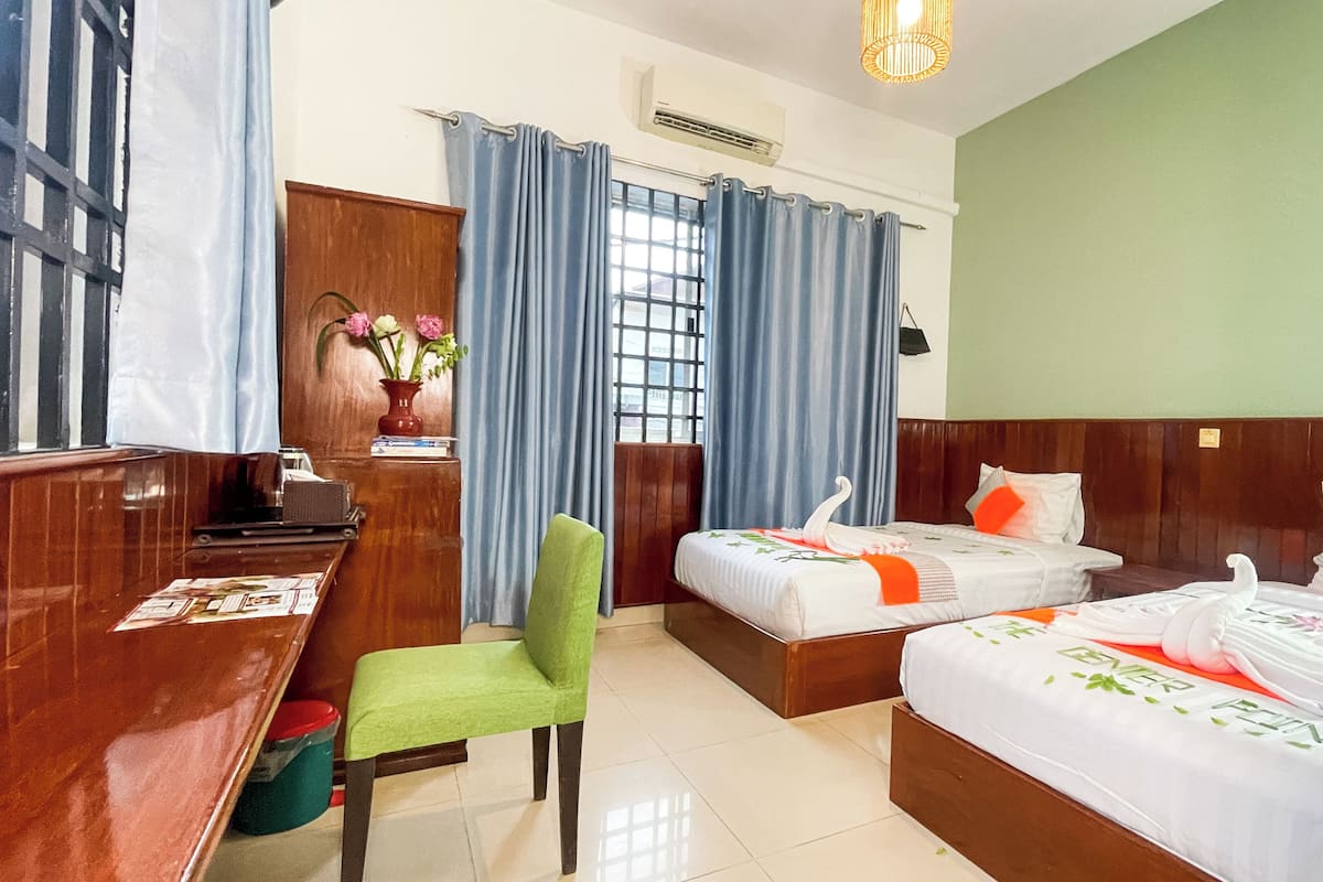 A hotel room with two beds, a desk, a chair, and a window with curtains.