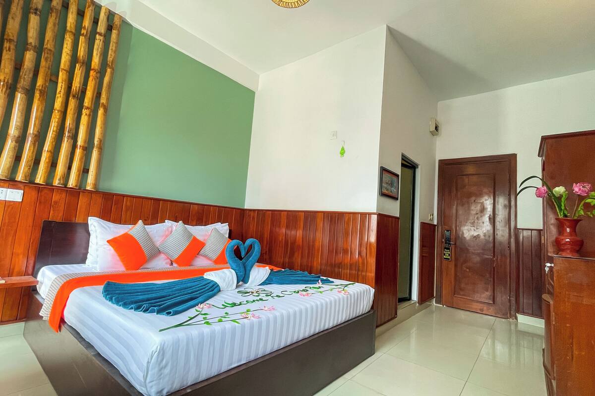 A hotel room with a wooden headboard, a bed with striped bedding, a nightstand, a wooden wardrobe, and a green wall.
