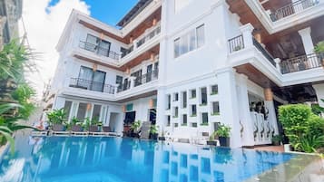 Un hotel de varios pisos con piscina, balcones y plantas en macetas.