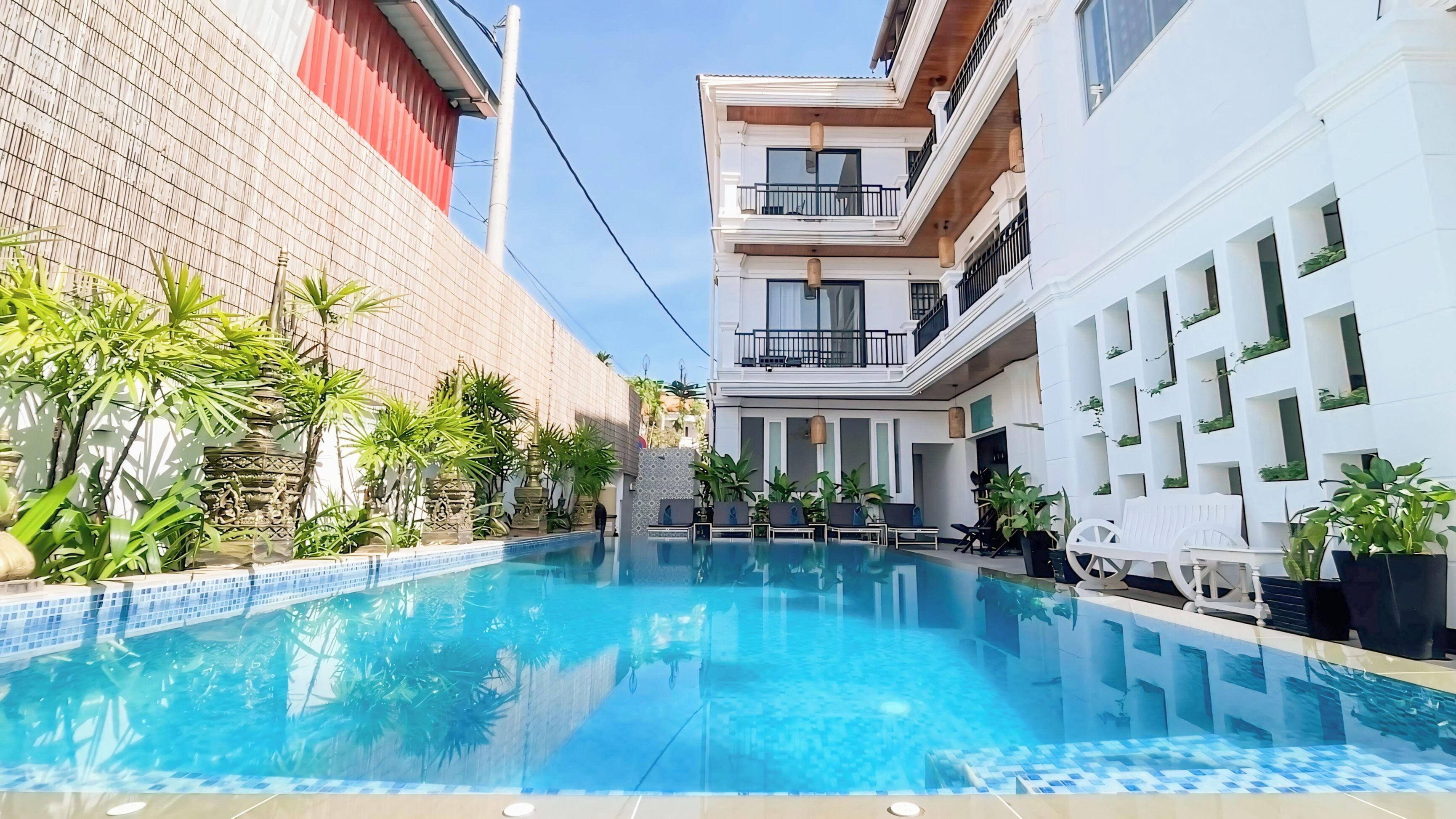 A swimming pool with clear blue water, surrounded by potted plants and outdoor furniture.