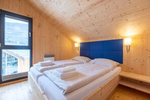 A wooden cabin bedroom with two beds, a window, and a view of the outside.