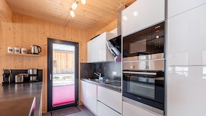 Une cuisine moderne avec des murs en bois, des appareils électroménagers en acier inoxydable et une vue sur l’extérieur, visible à travers la porte.