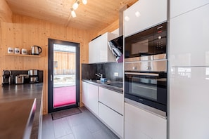 A modern kitchen with wooden walls, stainless steel appliances, and a view through the door.