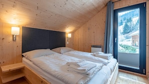 Une chambre dans un chalet en bois, avec deux lits, une fenêtre donnant sur un paysage enneigé et une étagère intégrée.