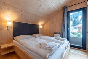 A wooden cabin room with two beds, a window with a view of a snowy landscape, and a built-in shelf.