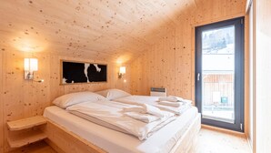 Ein Schlafzimmer einer Holzhütte mit einem Bett, zwei Nachttischen, einer Wandlampe und einem Fenster.