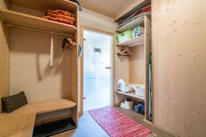 Una habitación pequeña con un banco, una puerta y estantes de madera con diversos objetos.