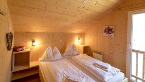 A wooden cabin room with two beds, a radio, and a painting on the wall.