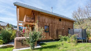 A wooden cabin with a balcony, a hot tub, and a trampoline in the yard.