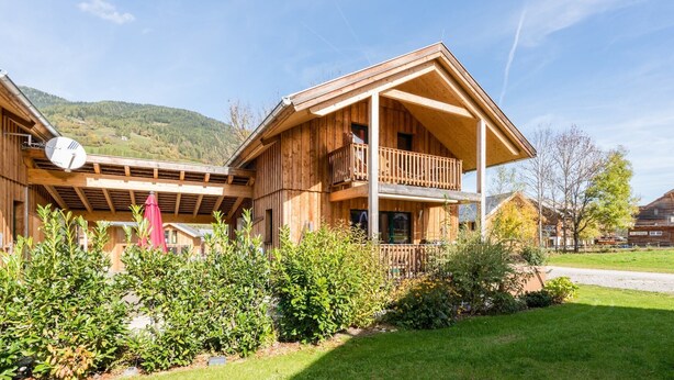 A wooden chalet with a balcony, surrounded by well-maintained gardens and a clear view of the mountains.