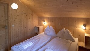 Una stanza con rivestimento in legno, due letti con biancheria da letto e cuscini bianchi, e due comodini a parete con lampade.