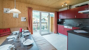 Una cucina moderna con mobili rossi, un'area pranzo con tavolo in legno apparecchiata per quattro persone e una porta vetrata scorrevole che dà su un balcone.